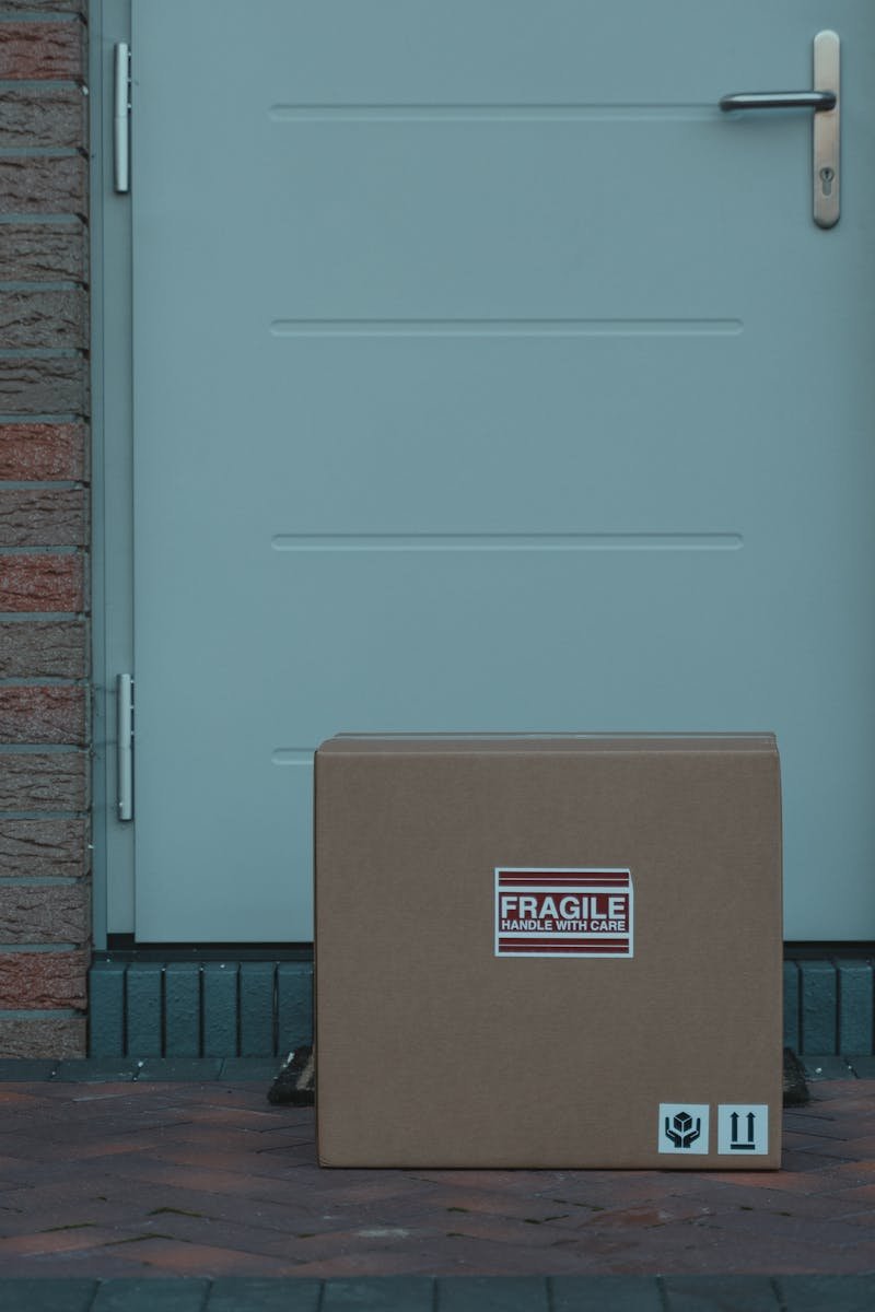 Cardboard box placed outside a brick-walled entrance, labeled fragile for delivery.
